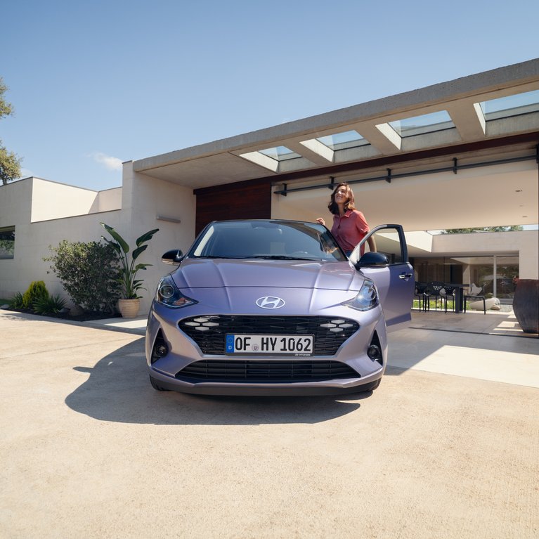 Hyundai Fahrzeug steht vor modernem Wohnhaus, Person steigt ein. Beispielbild für sofort verfügbare Vorführwagen und attraktive Angebote.
